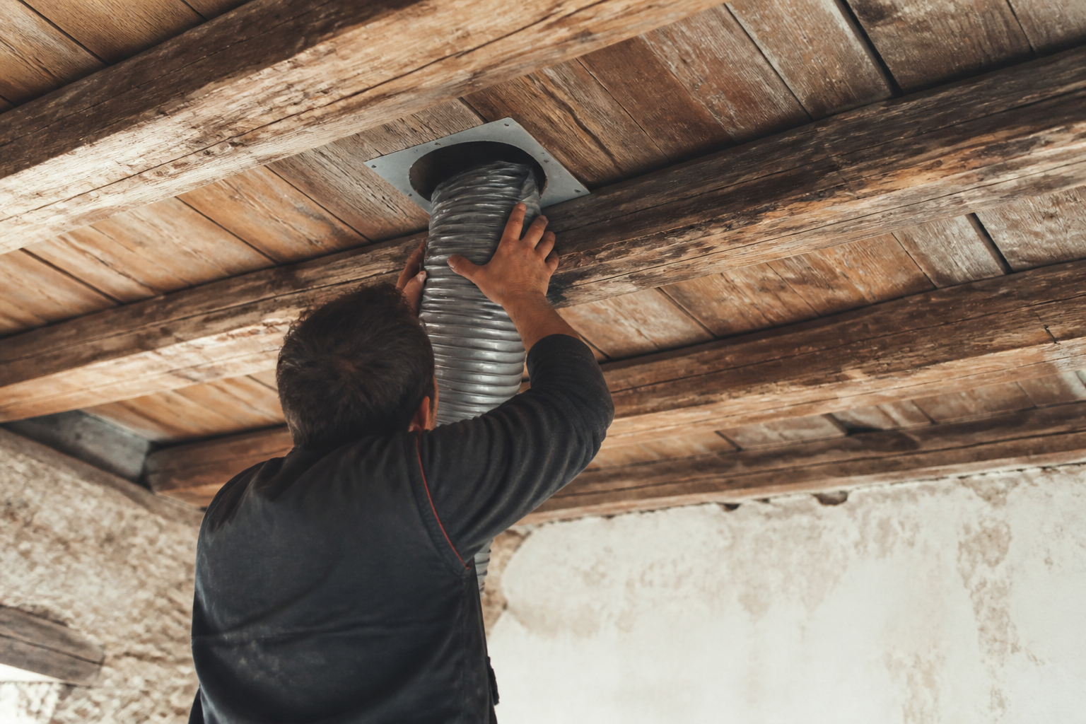 Technicien installant conduit ventilation traversant plafond ancien bois