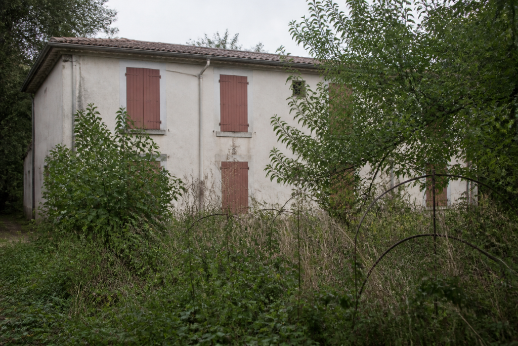 Maison vide avec fenêtres fermées et jardin abandonné